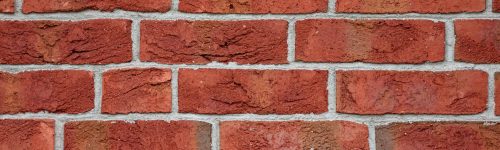 Finished Brick Veneer wall showing red bricks of different sizes separated by white grout